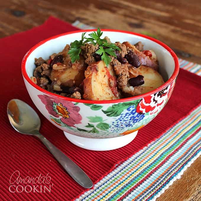 A multicolored bowl filled with cowboy casserole and a spoon on the side.