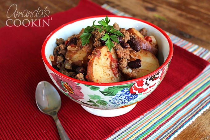 A multicolored bowl filled with cowboy casserole and a spoon on the side.