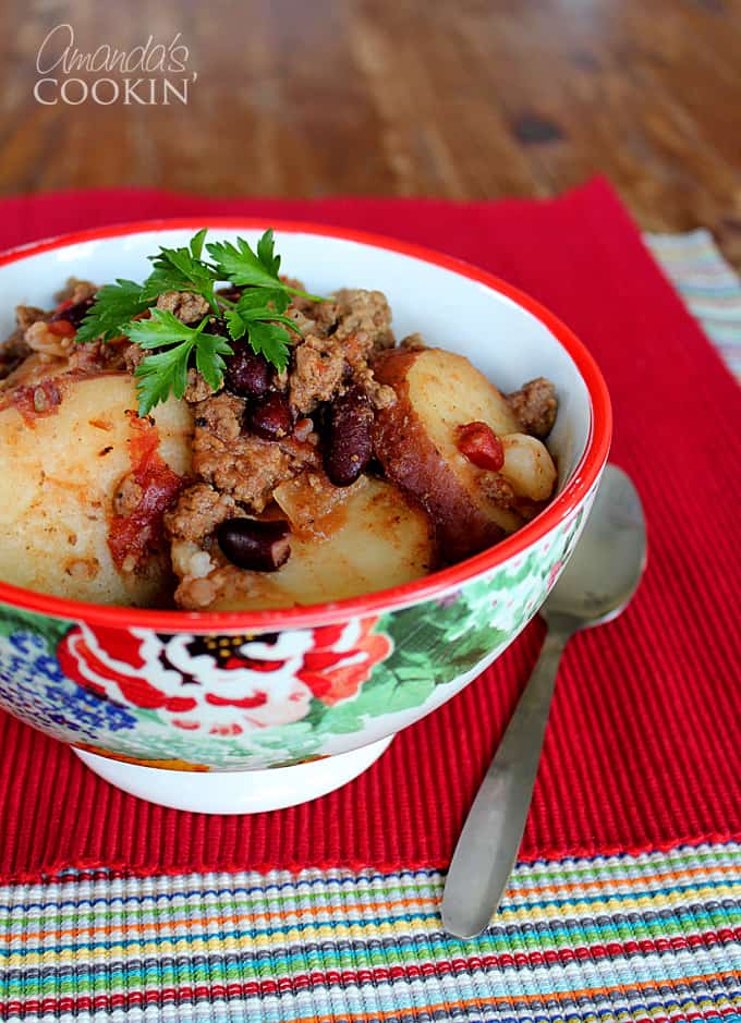 A close up of a multicolored bowl filled with cowboy casserole and a spoon on the side.