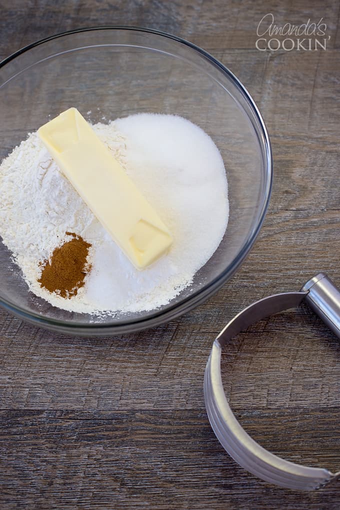 A clear bowl filled with flour, sugar, baking powder, salt, ground cinnamon and butter.