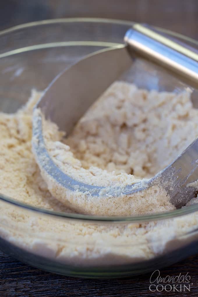 A clear bowl filled with the crumb mixture  and a pastry blender.