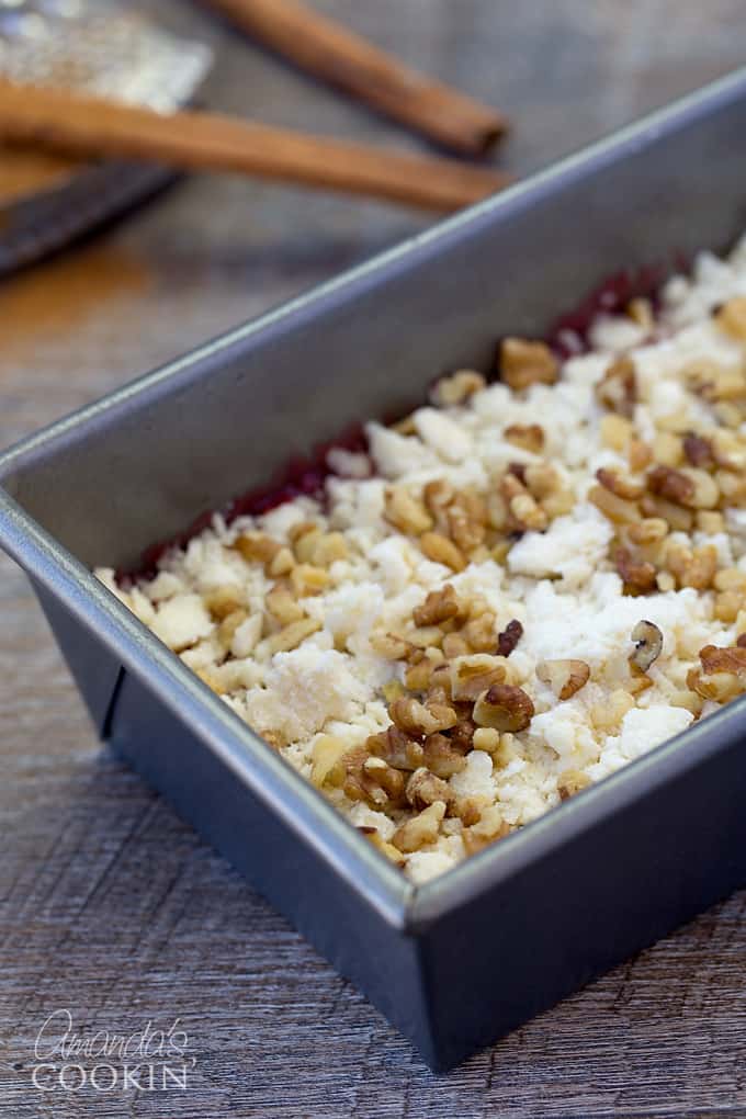 A close up of a loaf pan filled with batter, filling, crumb topping and nuts.