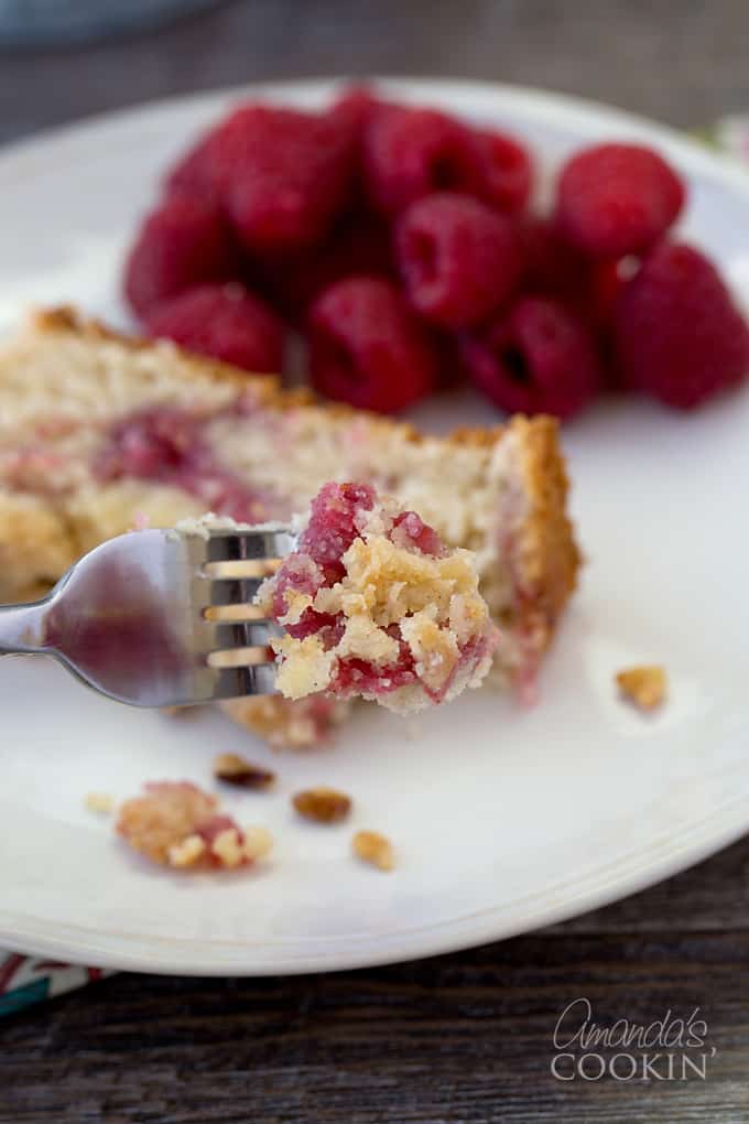 A forkful of raspberry coffee cake with raspberries and a slice of coffee cake in the background.