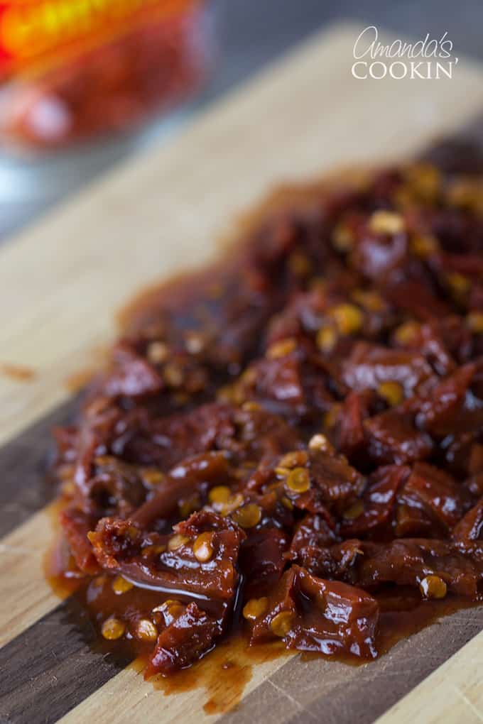 A close up of chopped chipotle chili peppers on a wooden cutting board.