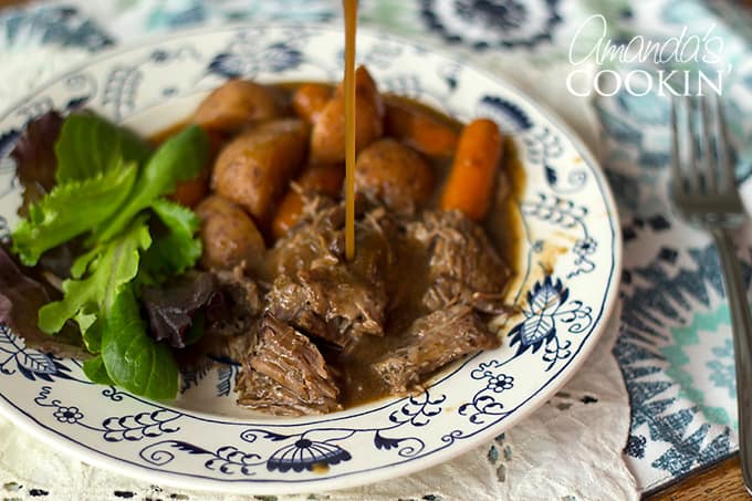 Gravy pouring onto crockpot roast beef and carrots