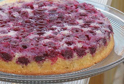 A close up photo of a raspberry upside down cake on a clear cake stand.