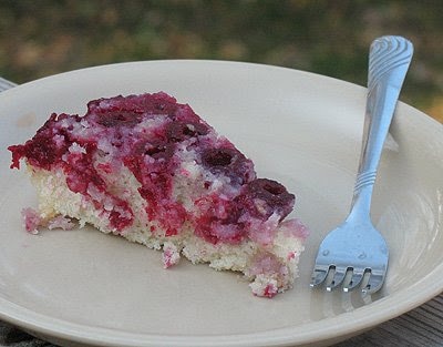 A close up photo of a slice of raspberry upside down cake on white plate served with a fork.