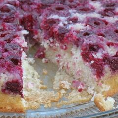 A close up photo of a raspberry upside down cake on a clear platter with a slice missing.