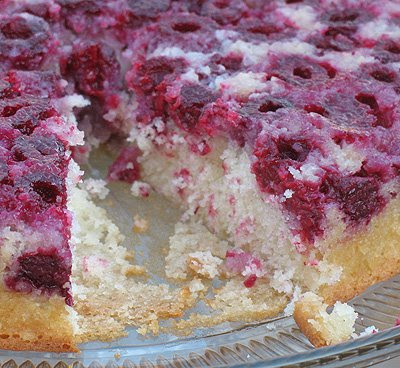 A close up photo of a raspberry upside down cake on a clear cake stand with a slice missing.