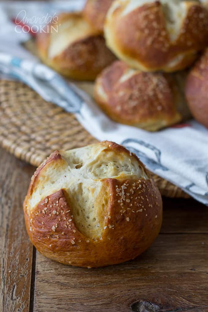 A close up of a bretzel roll with other rolls laying on a white and blue towel in the background.