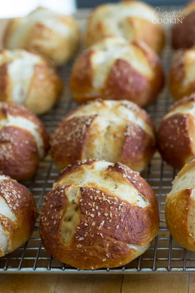 Three rows of bretzel rolls laying on a wire cooling rack.