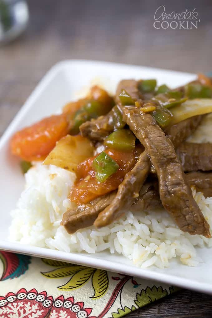 A close up of a white plate with rice and Chinese pepper steak on top.