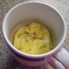 A close up overhead photo of scrambled eggs in a mug with pepper on top.