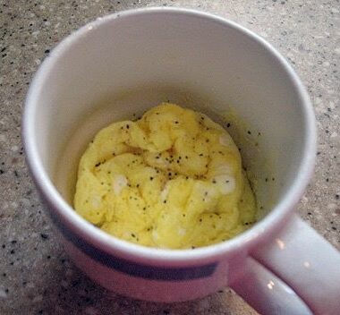 A close up overhead photo of scrambled eggs in a mug with pepper on top.