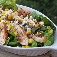 A close up photo of a grilled chicken salad with herbed tomato vinaigrette in a white dish.