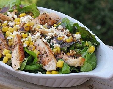A close up photo of a grilled chicken salad with herbed tomato vinaigrette in a white dish.