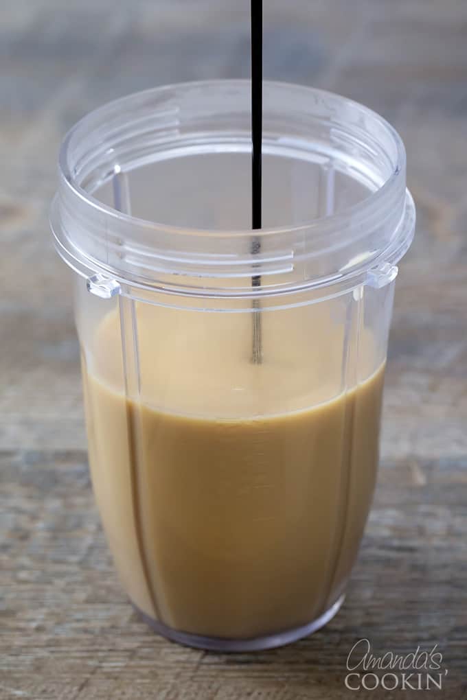 A blender cup with coffee filled halfway and chocolate sauce being drizzled in. 