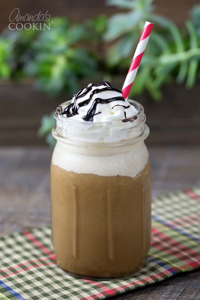 A mason jar filled with a mocha frappucino topped with whipped cream, chocolate sauce and a red stripped straw.