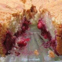 A close up photo of a cherry almond cake with a slice removed.