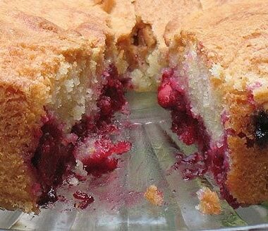 A close up photo of a cherry almond cake with a slice removed.