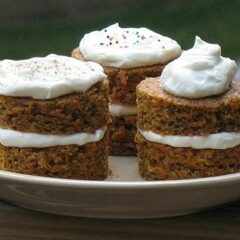 A close up photo of three carrot cake towers topped with fluffy cream cheese frosting.