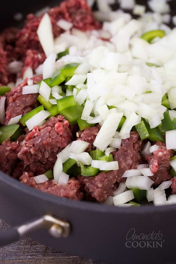 A close up of ground beef, chopped green bell pepper and chopped onion in a skillet.