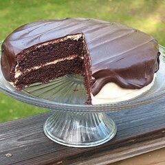 A photo of a chocolate cake with peanut butter frosting and chocolate peanut butter topping resting on a cake stand with a slice removed.