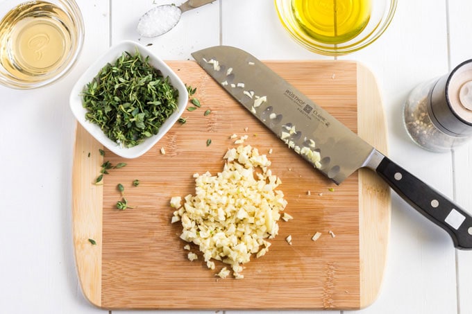 chopped garlic on cutting board with knife and fresh thyme