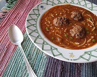 A close up photo of a bowl of Amanda's meatball soup with a spoon resting on the side.