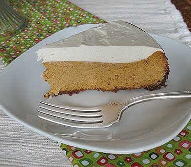 A slice of pumpkin cheesecake with rum whipped topping served on a white plate with a fork.