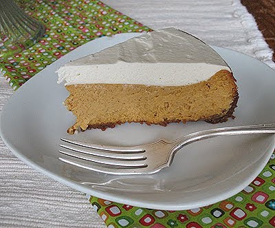 A slice of pumpkin cheesecake with rum whipped topping served on a white plate with a fork.