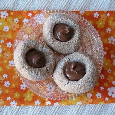 An overhead photo of three chocolate Nutella thumbprint cookies on a clear plate.