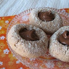 A close up photo of three chocolate Nutella thumbprint cookies on a clear plate.