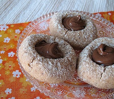 A close up photo of three chocolate Nutella thumbprint cookies on a clear plate.