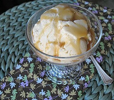 A close up picture of brown sugar vanilla bean ice cream in a clear bowl with caramel drizzle on top.