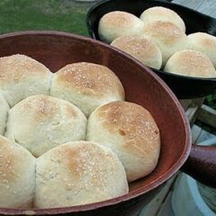 A close up photo of homemade dinner rolls in two cast iron skillets.
