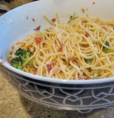 A close up photo of spaghetti with pancetta and broccoli in a bowl.