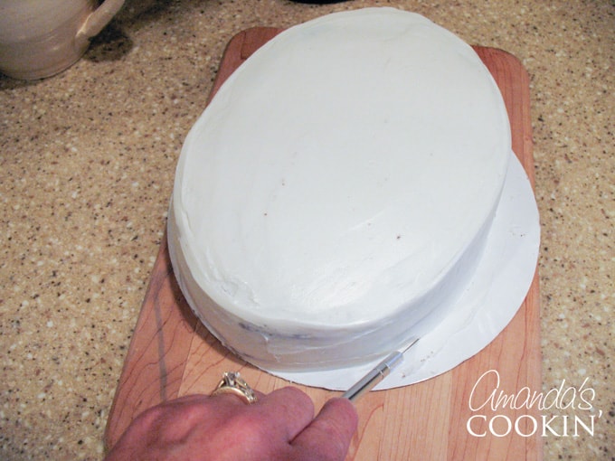 A close up photo of a cake resting on cardboard that is being cut with an x-acto knife.