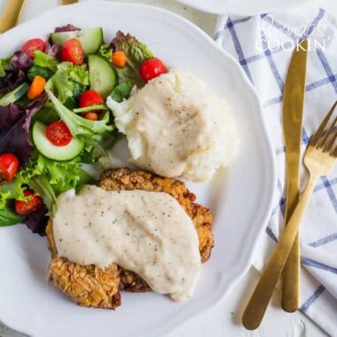 chicken fried steak with white gravy and salad on a plate