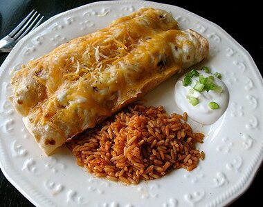 Shredded chicken and Chile enchiladas on a white plate with Spanish rice and sour cream on the side.