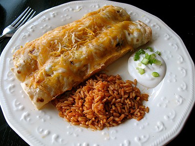 Shredded chicken and Chile enchiladas on a white plate with Spanish rice and sour cream on the side.