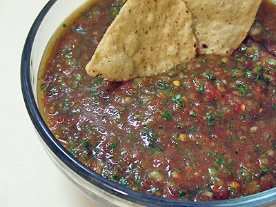 A close up photo of a bowl of homemade salsa with two tortilla chips resting on the side.