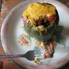 A close up photo of a forkful of chili and cornbread stuffed pepper with the whole stuffed pepper in the background.