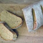 An overhead photo of a sliced loaf of rustic rosemary garlic bread resting on a wooden cutting board.