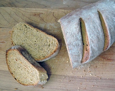 An overhead photo of a sliced loaf of rustic rosemary garlic bread resting on a wooden cutting board.