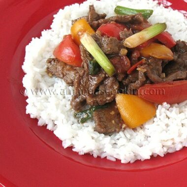 A photo of beef stir fry with tomatoes and peppers over rice.