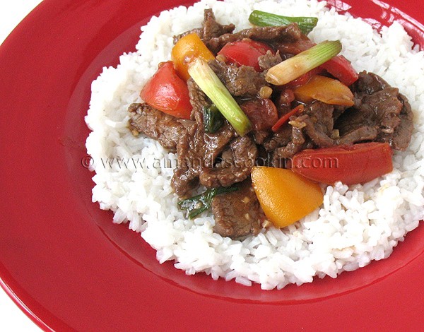 A photo of beef stir fry with tomatoes and peppers over rice.