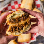hands holding a guinea grinder sandwich that has been cut in half