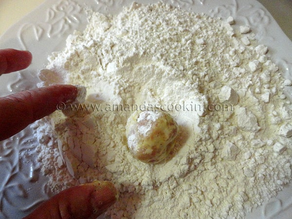 A photo of the chicken ball being rolled in the flour mixture again after being coated in egg.