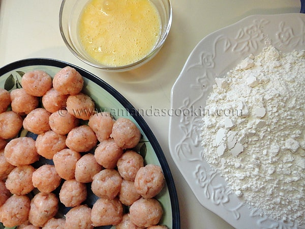 A photo of a plate of raw chicken balls, a bowl of whisked eggs and a plate of flour and salt.